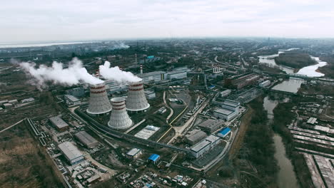 Aerial-View-Of-Industrial-Zone-With-Factories-Expelling-Smoke-Around-A-Green-Landscape