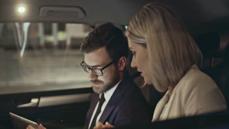 Outside-View-Of-A-Moving-Car,-A-Couple-In-Smart-Clothes-Talk-While-Looking-At-Smartphone