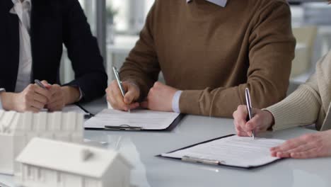 Camera-Focuses-Hands-Of-Business-People-Writing-On-Documents-On-The-Table