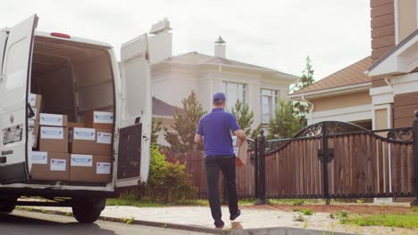 Rear-View-Of-A-Delivery-Man-Picking-Up-Cardboard-Boxes-From-A-Van-On-The-Street