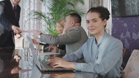Business-Woman-In-A-Business-Meeting-In-The-Office,-Uses-Laptop-While-Looking-At-Camera