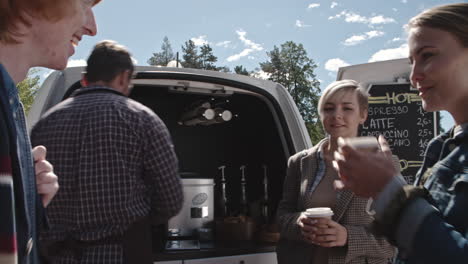 Group-Of-Young-People-Drinking-Coffee-And-Talking-With-An-Employee-Of-A-Coffee-Truck