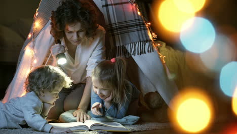 Mother-Reads-A-Book-Of-Fairy-Tales-For-Her-Children-While-Sitting-In-A-Tent-At-Night