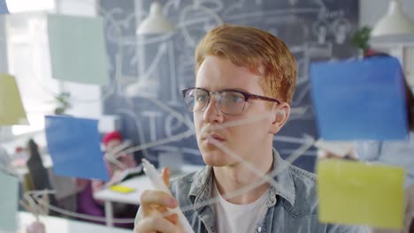 Red-Haired-Boy-In-Glasses-And-Casual-Clothes-Writing-Notes-On-The-Window-Glass