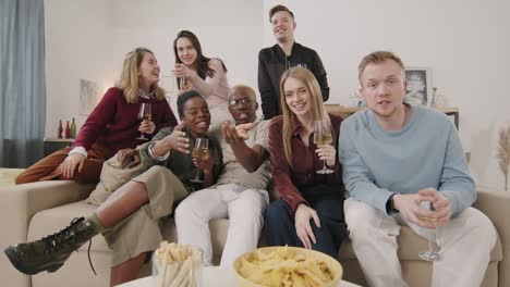 Group-Of-Friends-Sitting-On-Sofa,-Drinking-Wine-And-Waving-At-Camera-At-Home-Party