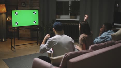 Rear-View-Of-A-Three-Friends-Sitting-On-The-Couch-Looking-At-A-Screen-And-Celebrating