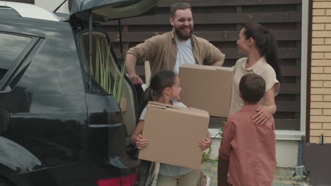 Family-With-Two-Children-Taking-Boxes-And-Personal-Items-From-Car-For-Moving