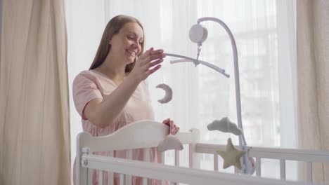 Pregnant-Woman-Approaches-Her-Baby's-Crib-And-Spinning-The-Toy