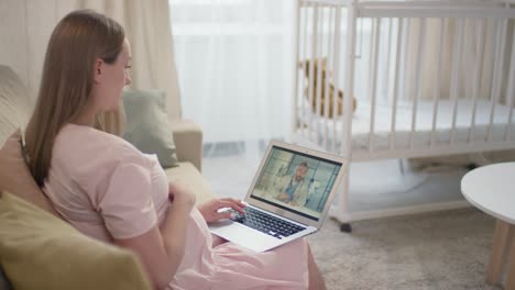 Mujer-Embarazada-Sentada-En-Un-Sofá-Y-Usando-Una-Laptop-En-Consulta-En-Línea-Con-Un-Médico