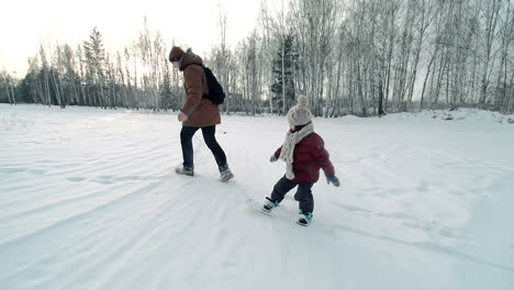 Vater-Und-Sohn-Im-Schnee-In-Winterkleidung,-Der-Vater-Schleppt-Das-Kind-Auf-Einem-Von-Einem-Seil-Gepackten-Snowboard-Nach-Draußen