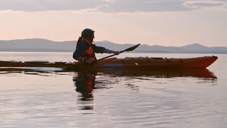 Side-View-Of-A-Man-With-Cap-And-Lifejacket-Paddling-A-Canoe-On-The-Lake-At-Sunset