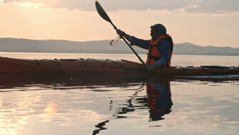 Side-View-Of-A-Man-With-Cap-And-Lifejacket-Paddling-A-Canoe-On-The-Lake-At-Sunset-1