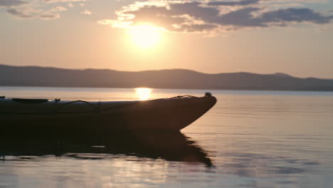 Nahaufnahme-Des-Sees-Und-Seitenansicht-Eines-Mannes-Mit-Mütze-Und-Schwimmweste,-Der-Bei-Sonnenuntergang-Ein-Kanu-Paddelt