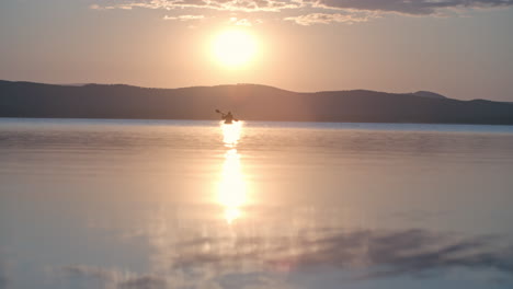 Distant-View-Of-A-Man-With-Cap-And-Lifejacket-Paddling-A-Canoe-On-The-Lake-At-Sunset