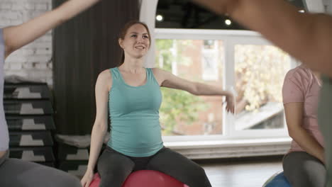 Camera-Focusing-On-A-Pregnant-Woman-In-Yoga-Class-Surrounded-By-Classmates