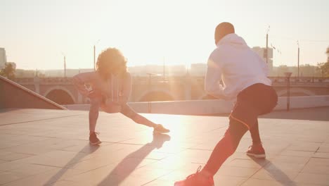 Couple-Wearing-Sportswear-Stretching-On-The-Street-At-Sunset