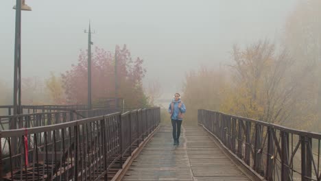 Blonde-Girl-With-Headphones-Running-On-A-Wooden-Bridge-On-A-Cloudy-Day