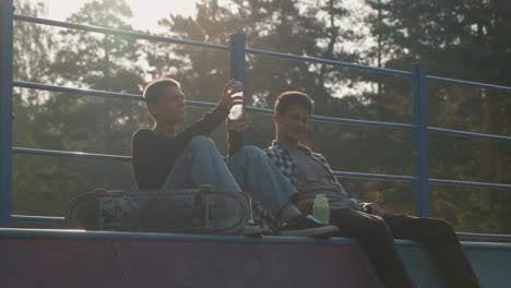 Zwei-Freunde-Sitzen-Im-Skatepark-Und-Unterhalten-Sich,-Während-Sie-Wasser-Trinken