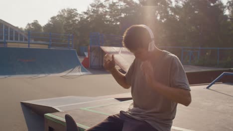 Junger-Mann-Im-Skatepark,-Der-Sich-Hinsetzt-Und-Kopfhörer-Aufsetzt