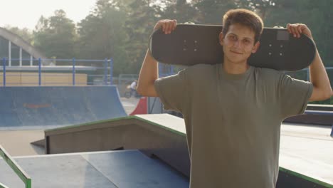 Young-Boy-In-Skatepark-Looking-At-Camera-Smiling-And-Holding-A-Scooter-Behind-His-Head
