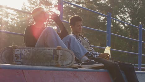Two-Friends-Sitting-In-Skate-Park-Talking-While-Drinking-Water-1