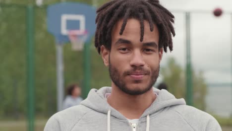 Junger-Lächelnder-Afroamerikanischer-Athlet-Mit-Dreadlocks,-Der-Den-Ball-Zum-Basketballspielen-Auf-Dem-Basketballplatz-Hält