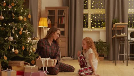 Mother-Waits-For-Her-Daughter-Sitting-Under-The-Christmas-Tree-In-The-Living-Room-While-Girl-Runs-And-Hugs-Her-Mother