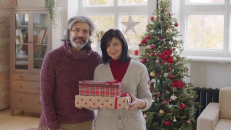 Couple-Looks-At-The-Camera-And-Smiles-While-Holding-Christmas-Presents