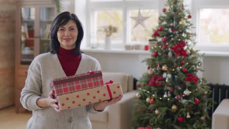 Brunette-Woman-In-Casual-Clothes-Looks-At-Camera-And-Smiles-While-Holding-Christmas-Gifts
