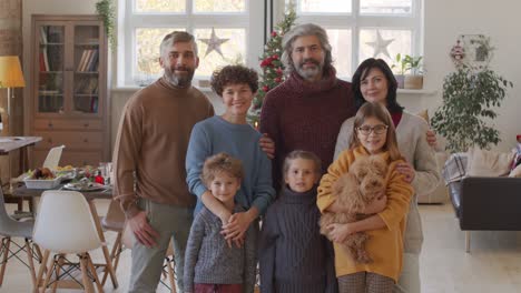 Lächelnde-Familie,-Die-Kamera-Im-Wohnzimmer-Mit-Tisch--Und-Weihnachtsdekorationen-Betrachtet