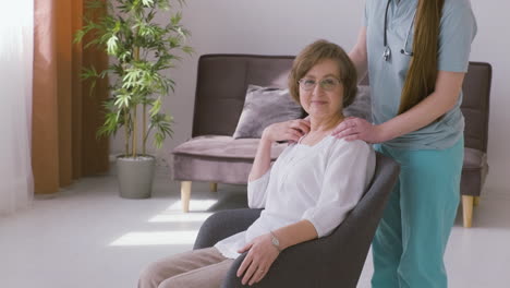 Senior-Woman-Sitting-On-A-Sofa-And-Female-Doctor-Putting-Hands-On-Her-Shoulders