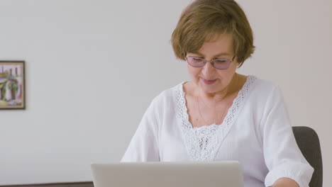 Senior-Woman-With-Eyeglasses-Sitting-On-A-Sofa-Using-Tablet