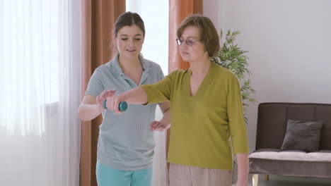 Elder-Woman-Holding-A-Dumbbell-Raising-An-Arm-Up-Assisted-By-A-Female-Doctor