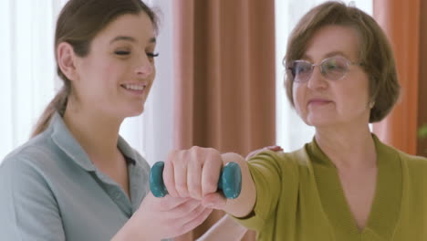 Elder-Woman-Holding-A-Dumbbell-Raising-An-Arm-Up-Assisted-By-A-Female-Doctor-3