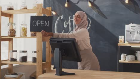 Camarera-Musulmana-En-Un-Café,-Pone-Un-Café-Para-Llevar-Encima-De-La-Caja-Registradora