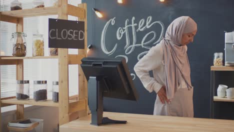 Woman-Waitress-In-A-Cafeteria-Hangs-The-Closed-Signboard-And-Takes-Off-Her-Apron-Behind-The-Counter