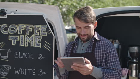 Coffee-Truck-Worker-Leaning-On-The-Van-While-Using-A-Tablet