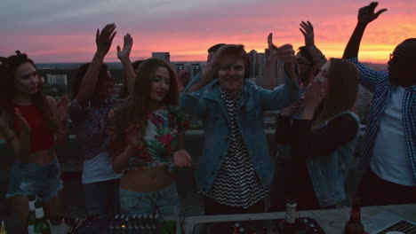 Group-Of-Friends-Enjoying-A-Party-On-A-Terrace-At-Sunset,-Everyone-Cheers-The-Dj
