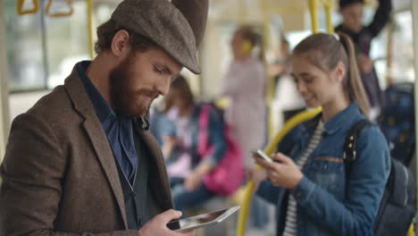 Young-Man-With-Beret-Using-Smartphone-Standing-In-The-Bus,-In-The-Background-A-Young-Girl-Standing-Chatting-With-Smartphone