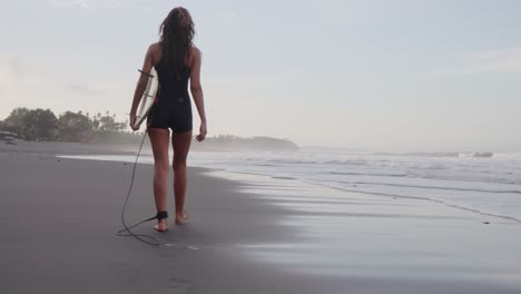 Back-View-Of-A-Sporty-Woman-Walking-On-A-Sandy-Beach-With-Her-Surfboard