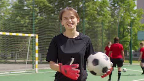 Young-Female-Soccer-Player-With-Ball-Smiling-And-Looking-At-Camera-On-The-Field