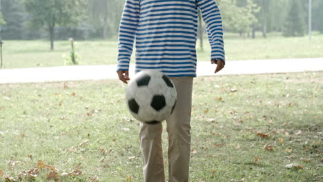Junge-Mit-Kurzen-Haaren-Und-Gestreiftem-Hemd-Tritt-Fußball-Und-Berührt-Ihn-Mit-Dem-Kopf-Im-Park