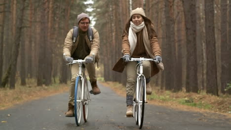 Front-View-Of-A-Couple-Wearing-Winter-Clothes-Riding-Bikes-In-The-Forest-While-Raining-1