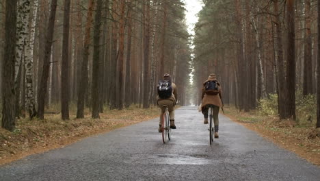 Rear-View-Of-A-Couple-Wearing-Winter-Clothes-Riding-Bikes-In-The-Forest-While-Raining
