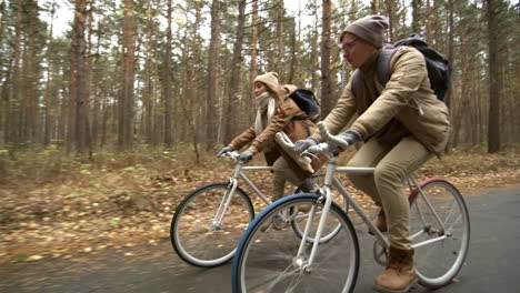 Side-View-Of-A-Couple-Wearing-Winter-Clothes-Riding-Bikes-In-The-Forest-While-Raining