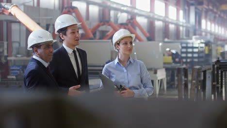 Two-Businessmen-And-Business-Woman-Dressed-In-Smart-Clothes-And-Helmets-In-A-Factory