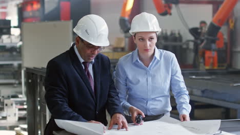 Engineers-In-Elegant-Clothes-And-Helmets-Consulting-About-Details-Of-Sketch-On-Blueprint-At-Meeting