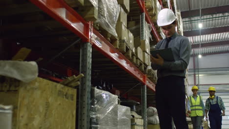Businessman-In-Elegant-Clothes-In-Warehouse-Sorting-Big-Boxes-While-Standing-In-Aisle-By-Huge-Shelf-With-Packed-Goods