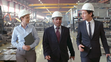 Engineers-In-Elegant-Clothes-And-Helmets-Walking-On-Corridor-In-A-Factory-Discussing-Details-About-Business