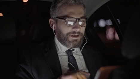 Businessman-With-Gray-Hair,-Glasses-And-Stylish-Clothes-Greets-On-A-Video-Call-While-Traveling-By-Car